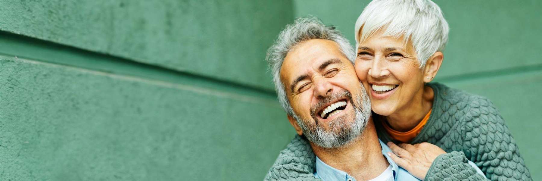 An elderly couple smiling broadly against a green wall in Arkansas