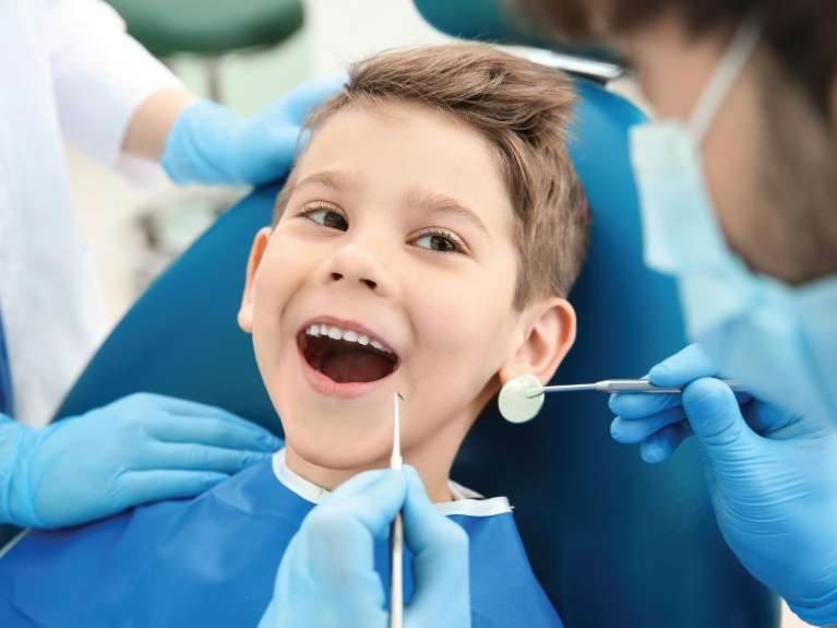 A young boy sitting in a dental chair with his mouth open.